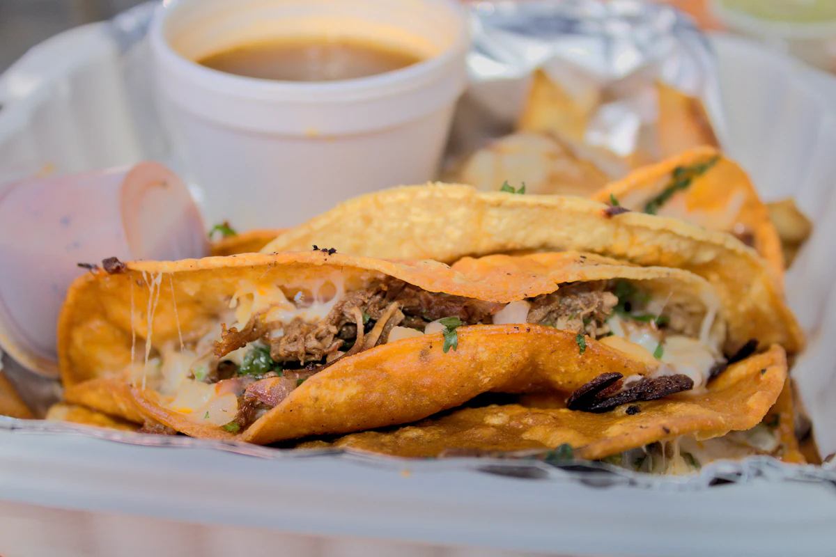 Crisp folded tacos with melted cheese and a pot of broth for dipping