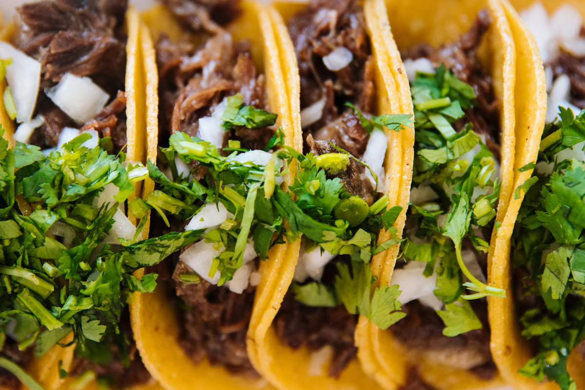 A row of beef tacos topped with chopped onion and coriander