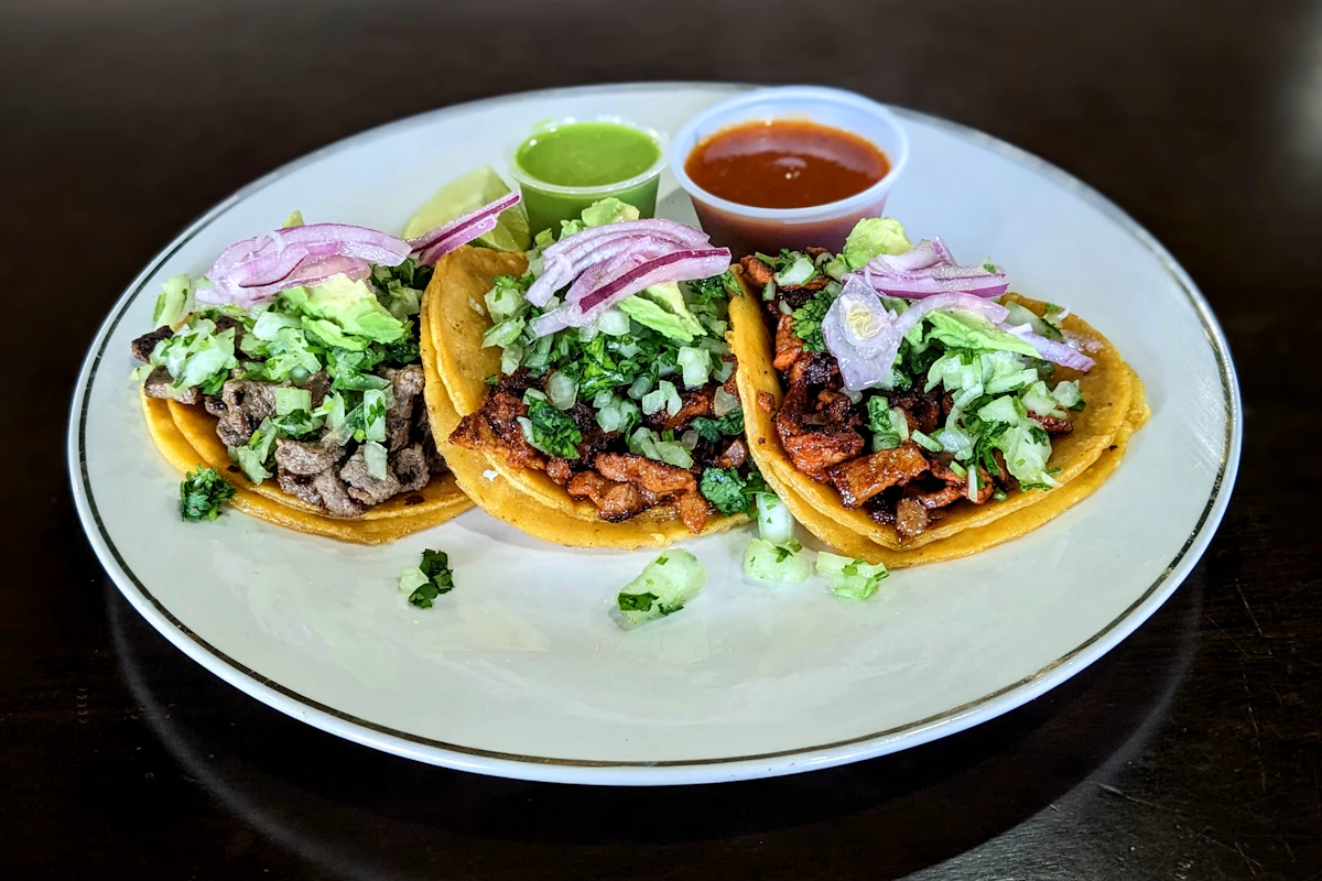 Three street tacos with red onion, salsa and lime on a white plate