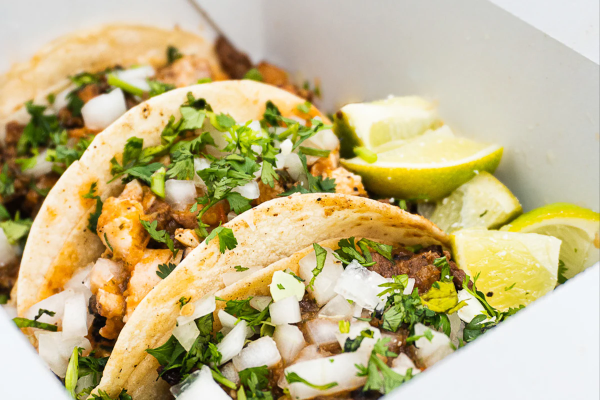 Tacos topped with onion, coriander and lime in a white takeaway box